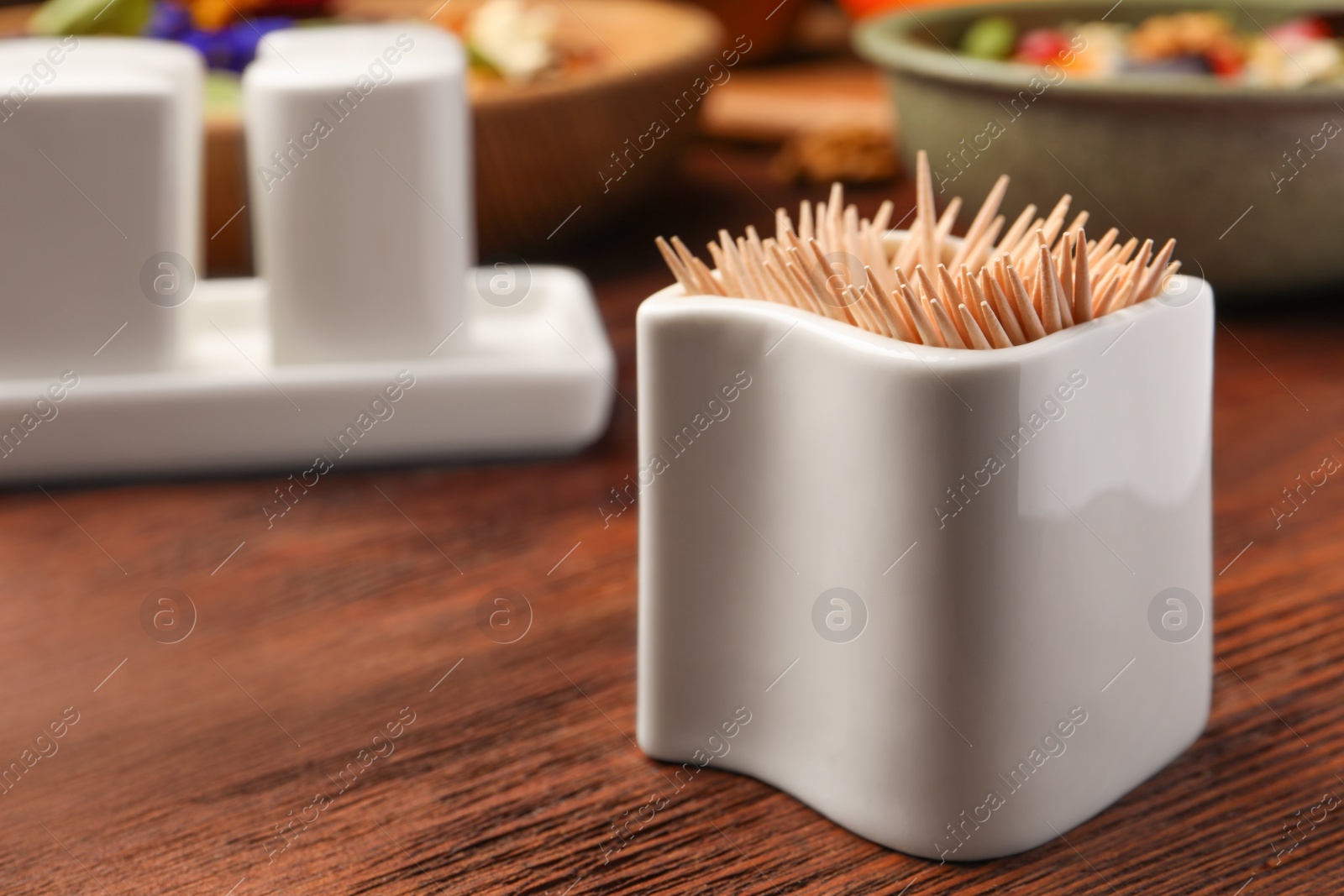 Photo of Holder with many toothpicks on wooden table, closeup. Space for text