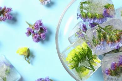 Photo of Bowl of ice cubes with flowers on blue background, top view. Space for text