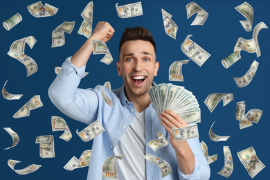 Happy young man with dollars under money rain on blue background