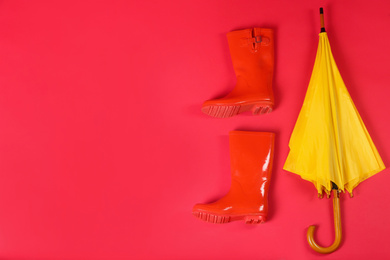 Photo of Beautiful yellow umbrella and rubber boots on red background, flat lay. Space for text