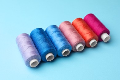 Photo of Set of different colorful sewing threads on light blue background