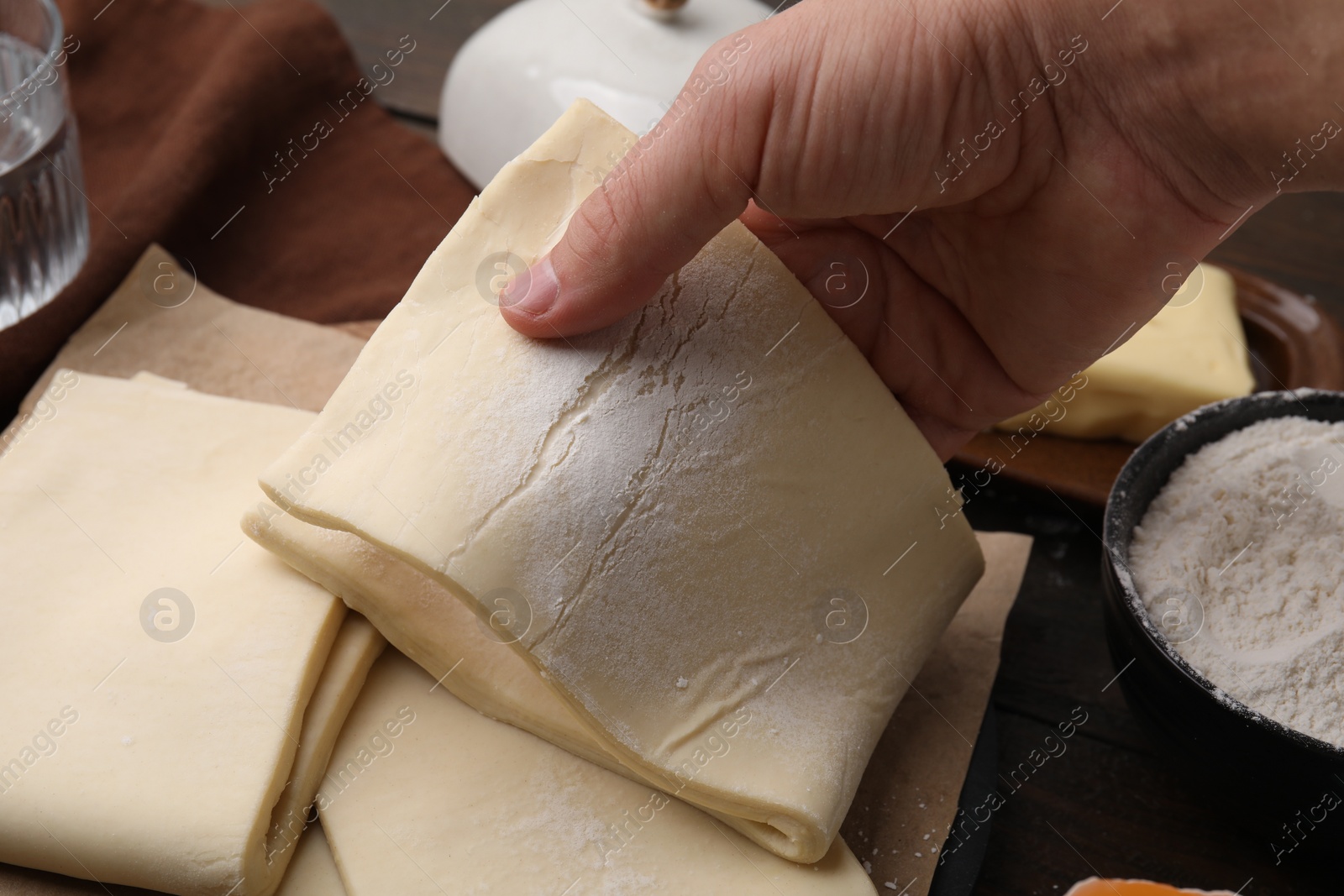 Photo of Man holding raw puff pastry dough at wooden table, closeup