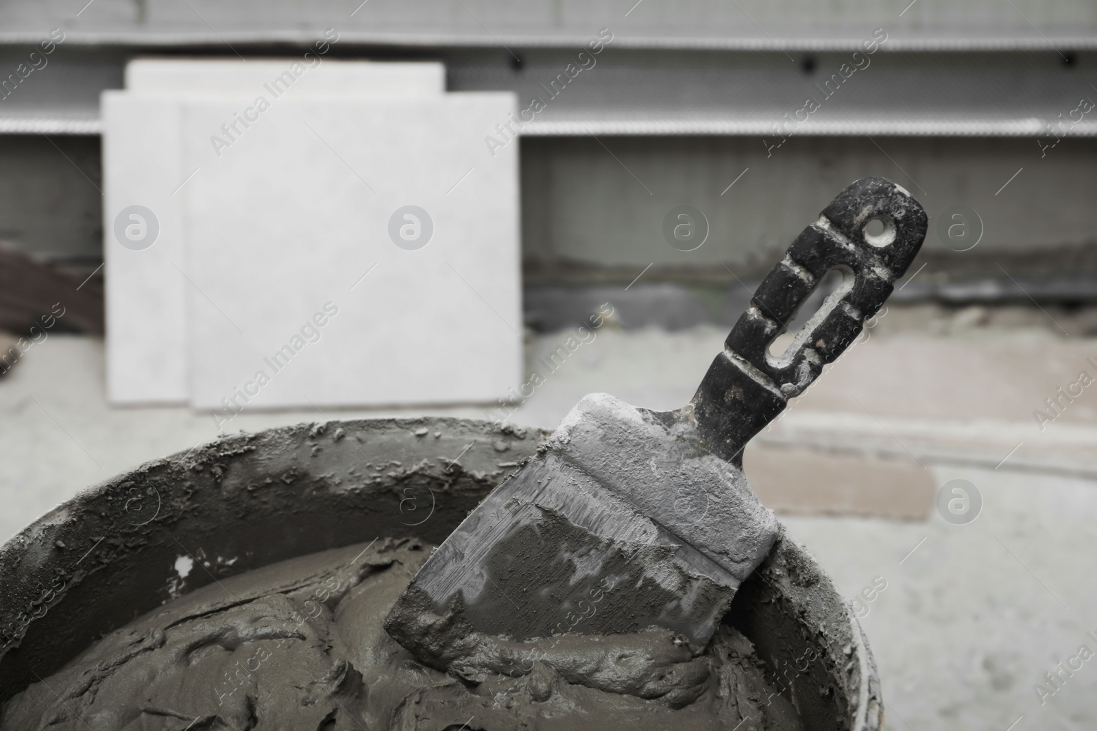 Photo of Adhesive mix, spatula and ceramic tiles on floor, closeup