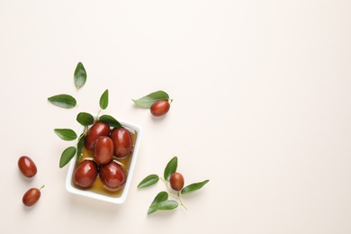 Photo of Sauce boat with jojoba oil and seeds on light background, flat lay. Space for text