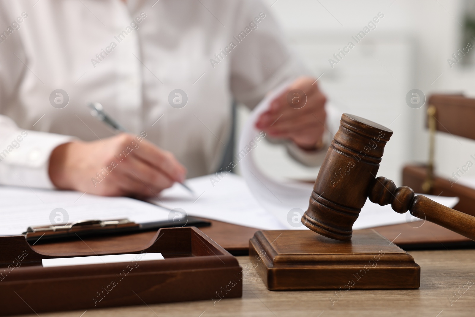 Photo of Lawyer working with documents at wooden table in office, focus on gavel