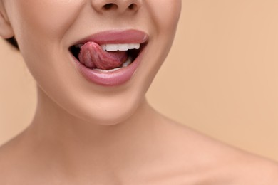 Woman with beautiful lips licking her teeth on beige background, closeup