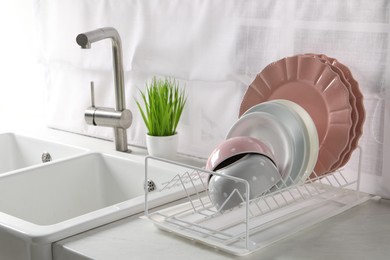 Photo of Drainer with different clean dishware on white table in kitchen