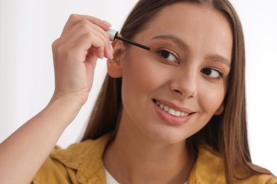 Photo of Beautiful woman applying serum onto eyelashes near mirror indoors, closeup