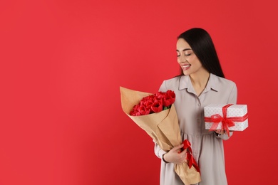 Photo of Happy woman with tulip bouquet and gift box on red background, space for text. 8th of March celebration