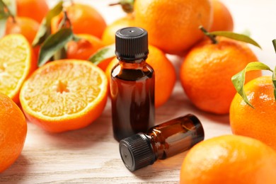 Photo of Bottles of tangerine essential oil and fresh fruits on wooden table, closeup