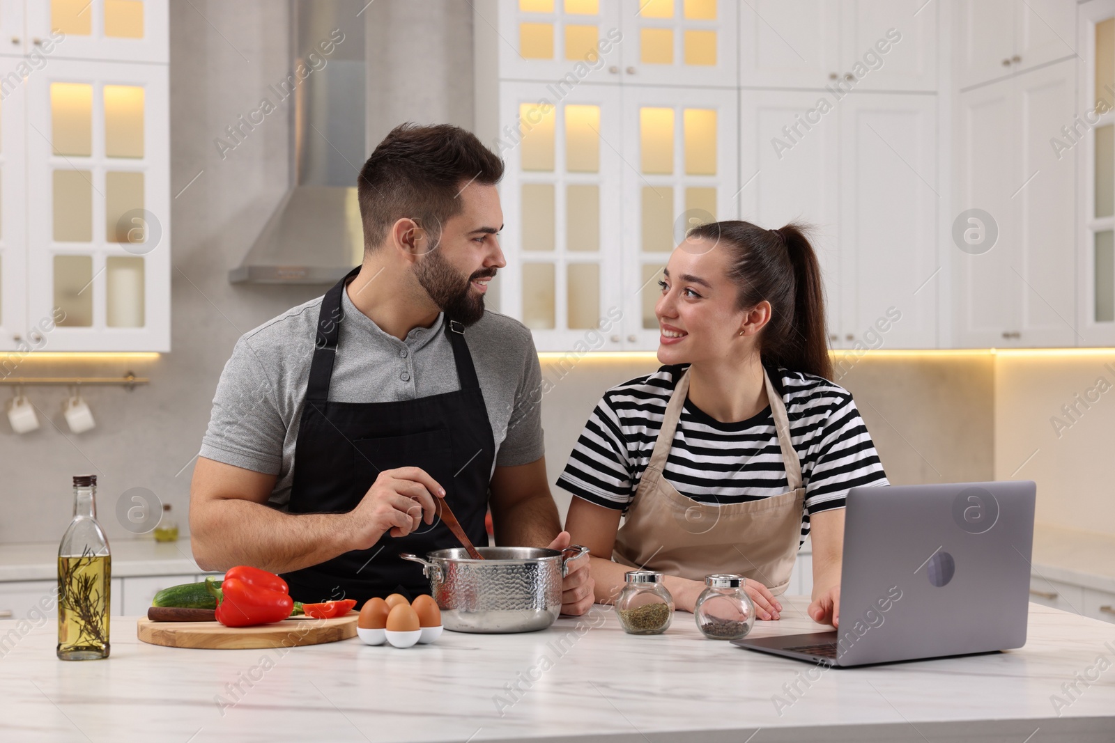 Photo of Happy lovely couple using laptop while cooking in kitchen