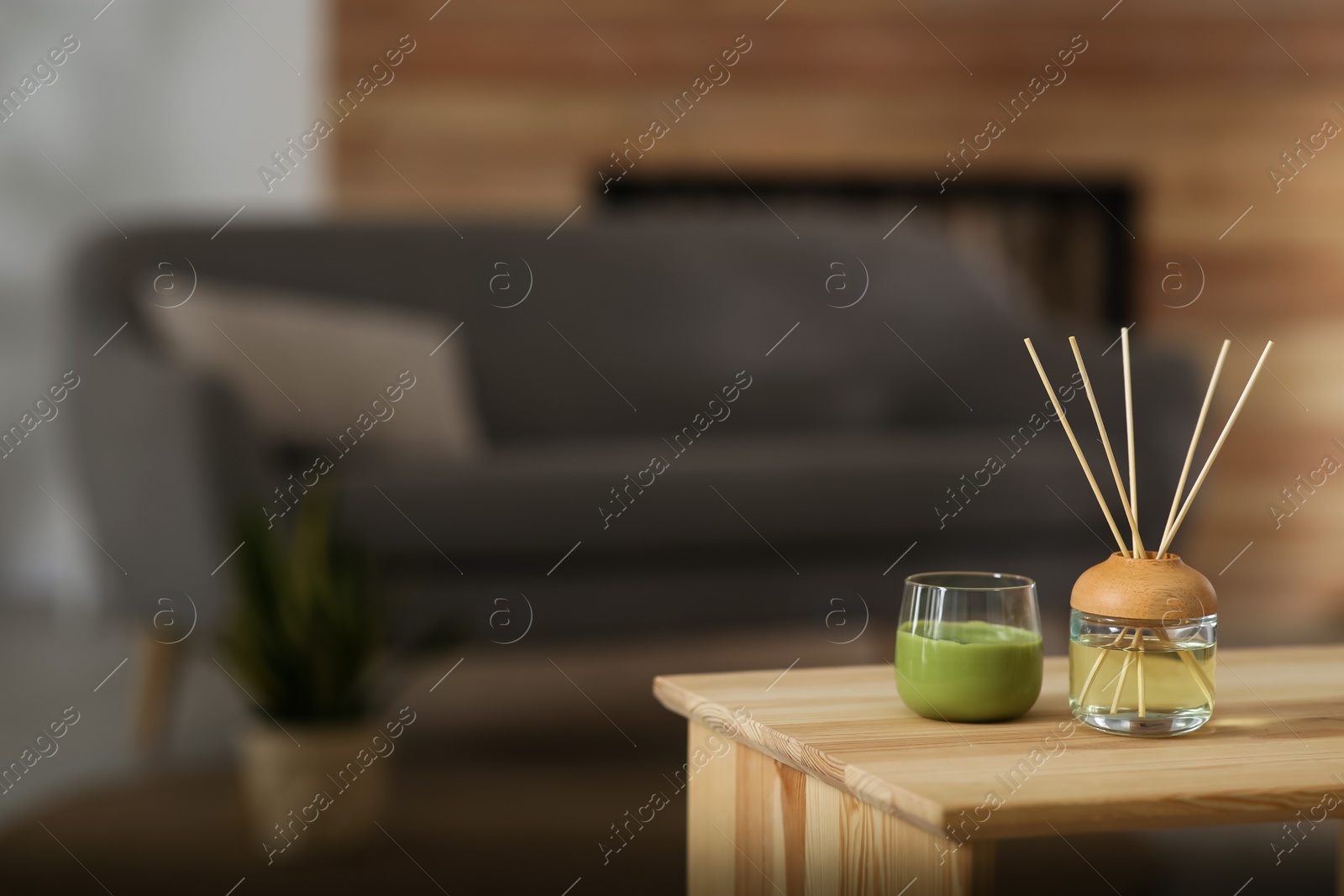 Photo of Aromatic reed air freshener and scented candle on table indoors. Space for text