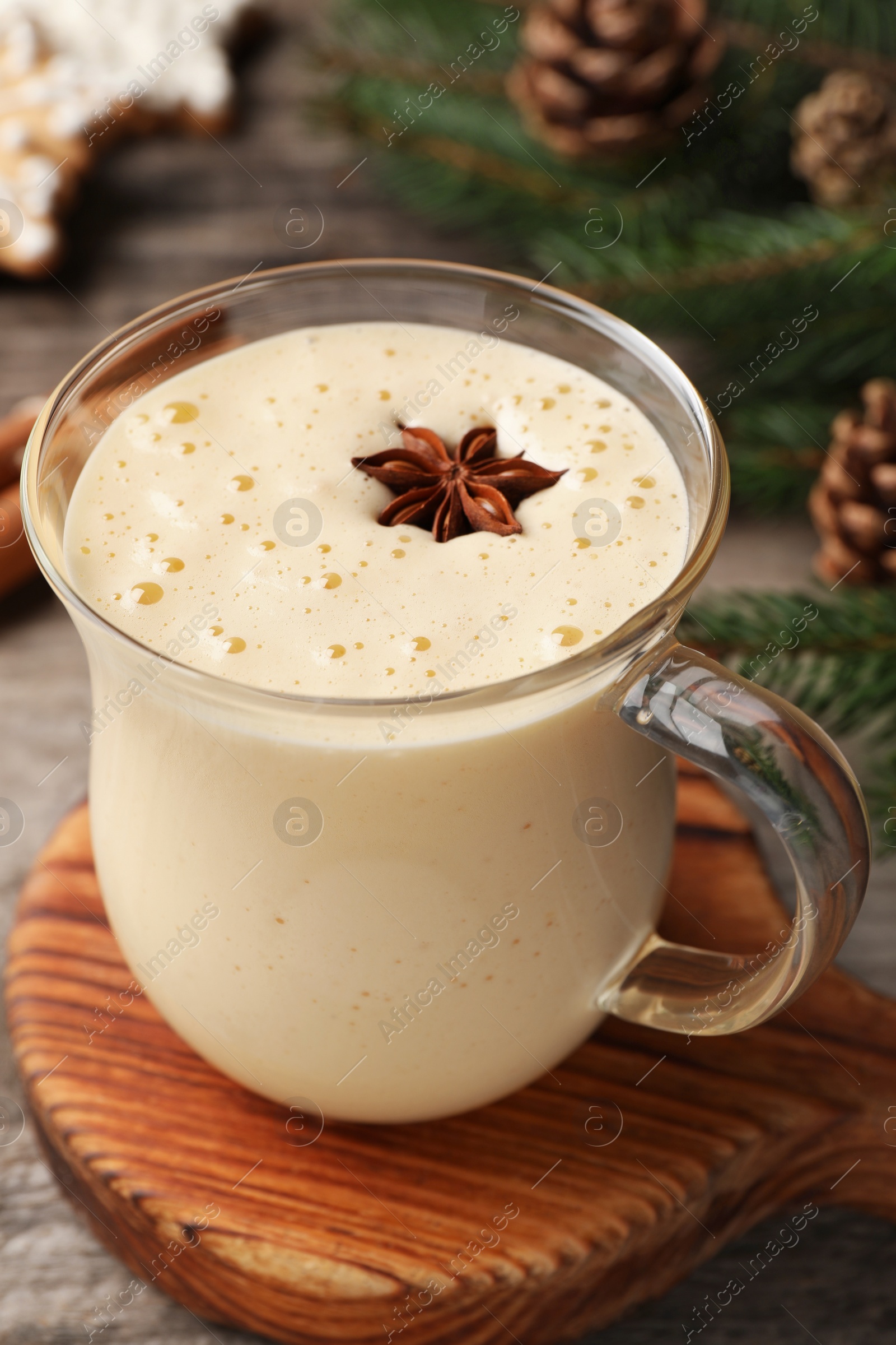 Photo of Glass of delicious eggnog with anise star on wooden table, closeup