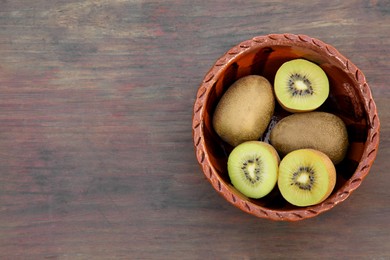 Photo of Bowl of whole and cut fresh kiwis on wooden table, top view. Space for text