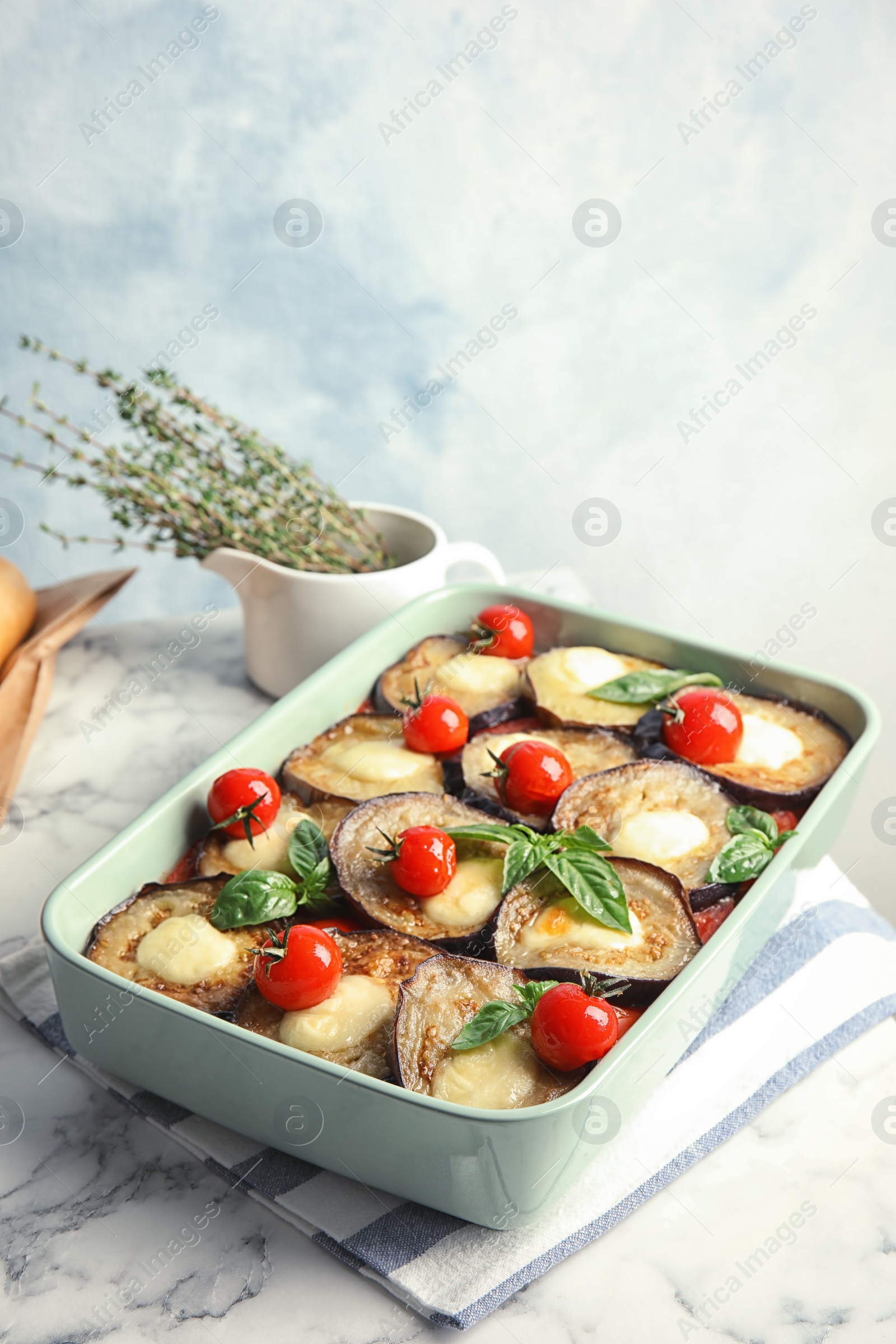 Photo of Baked eggplant with tomatoes, cheese and basil in dishware on marble table