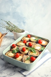 Baked eggplant with tomatoes, cheese and basil in dishware on marble table