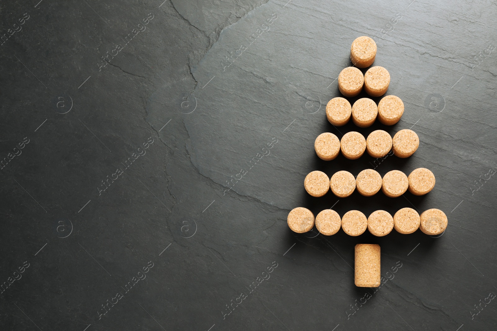 Photo of Christmas tree made of wine corks on dark stone background, top view. Space for text