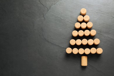 Photo of Christmas tree made of wine corks on dark stone background, top view. Space for text