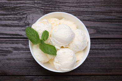 Photo of Delicious vanilla ice cream and mint in bowl on wooden table, top view