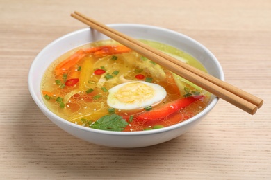 Photo of Bowl of tasty ramen with noodles, vegetables and chopsticks on wooden table