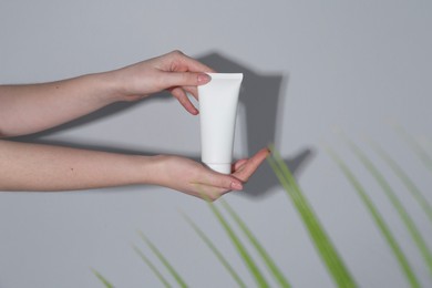 Photo of Woman holding tube of cream on grey background, closeup