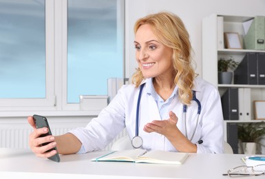 Photo of Doctor with smartphone and notebook consulting patient in clinic. Online medicine concept