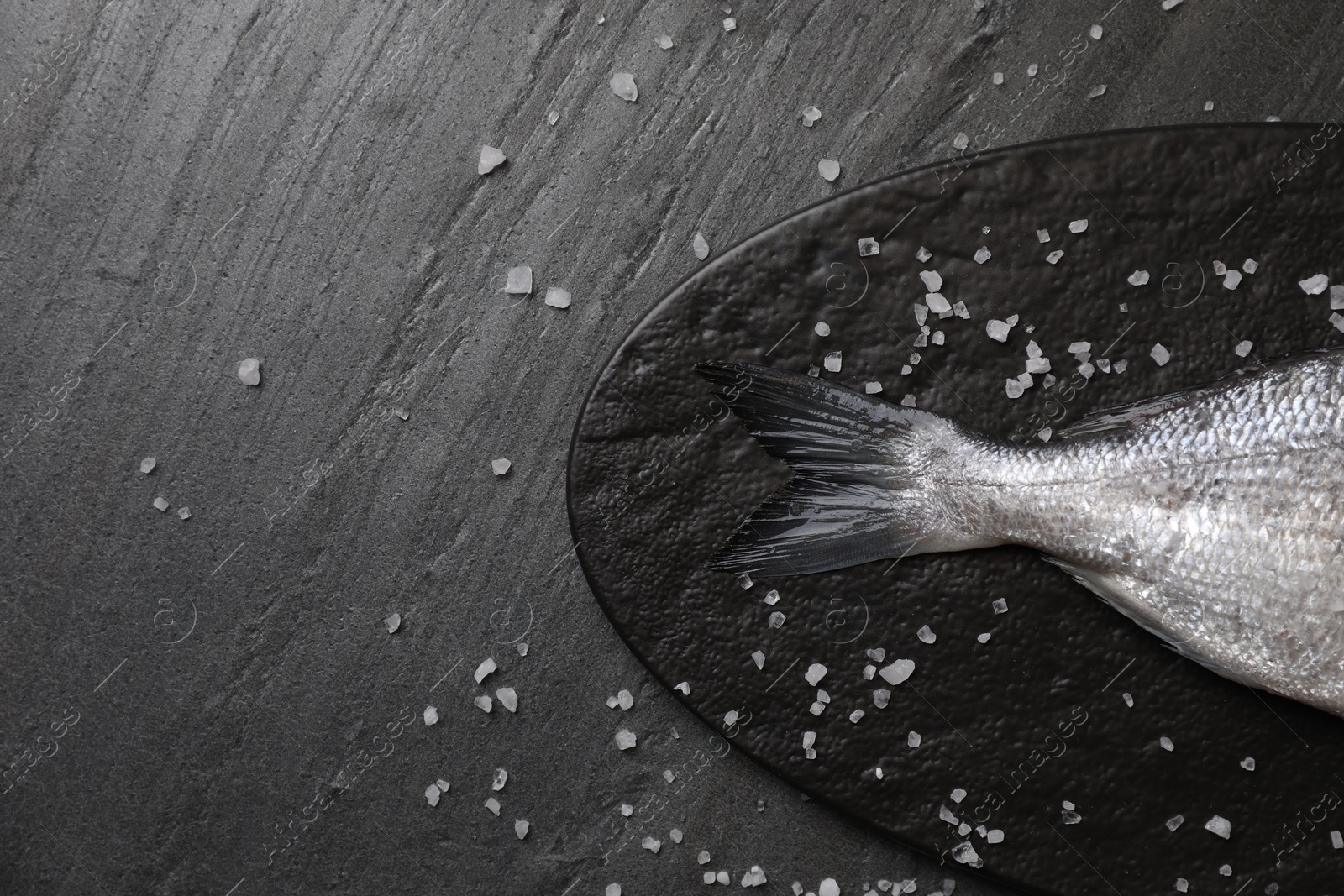 Photo of Fresh raw dorado fish and sea salt on black table, flat lay. Space for text