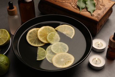 Photo of Bowl of essential oil with lemons on grey table. Aromatherapy treatment