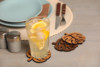 Glass of lemonade and leaf shaped cup coasters on grey wooden table