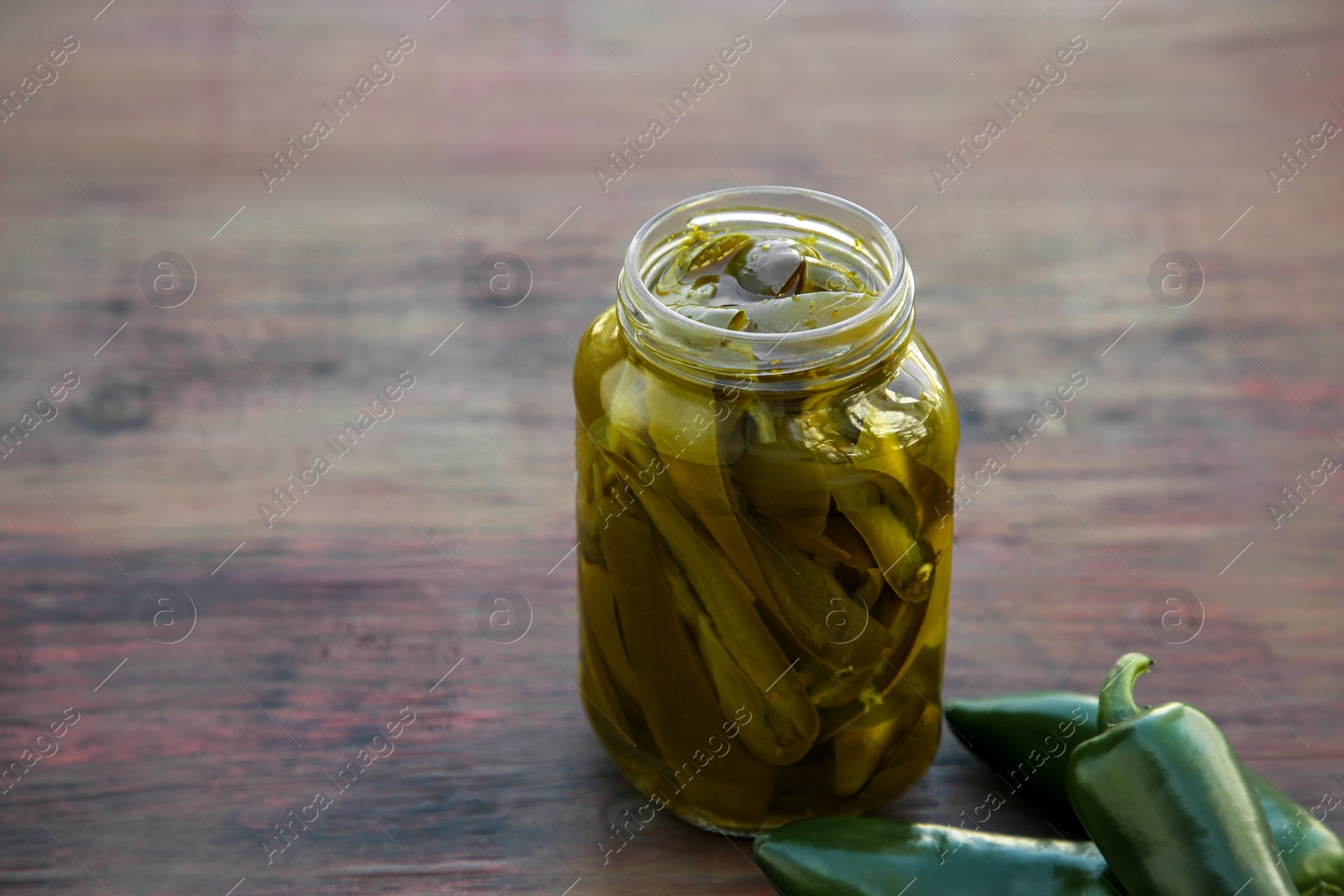 Photo of Fresh and pickled green jalapeno peppers on wooden table. Space for text