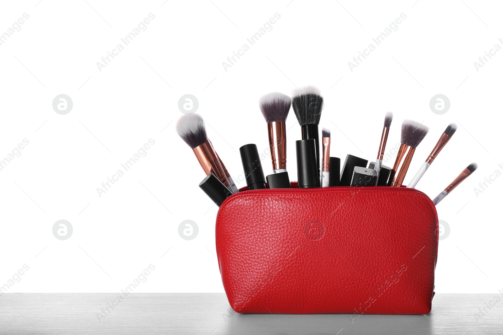 Photo of Bag with makeup brushes and cosmetic products on grey table against white background. Space for text