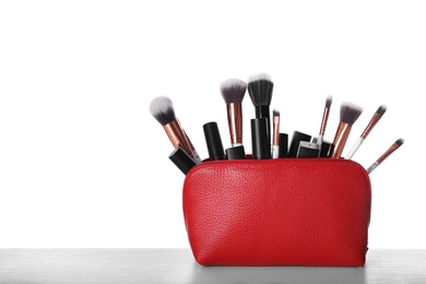 Bag with makeup brushes and cosmetic products on grey table against white background. Space for text
