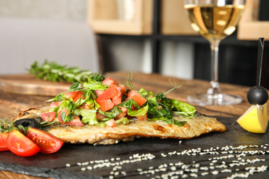 Photo of Delicious grilled fish with vegetables on slate plate, closeup