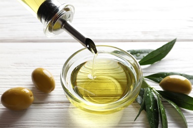 Pouring fresh olive oil into bowl on table