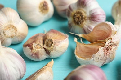 Photo of Fresh unpeeled garlic bulbs and cloves on light blue wooden table, closeup. Organic product