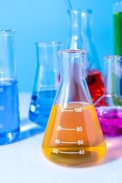 Different laboratory glassware with colorful liquids on white table against light blue background