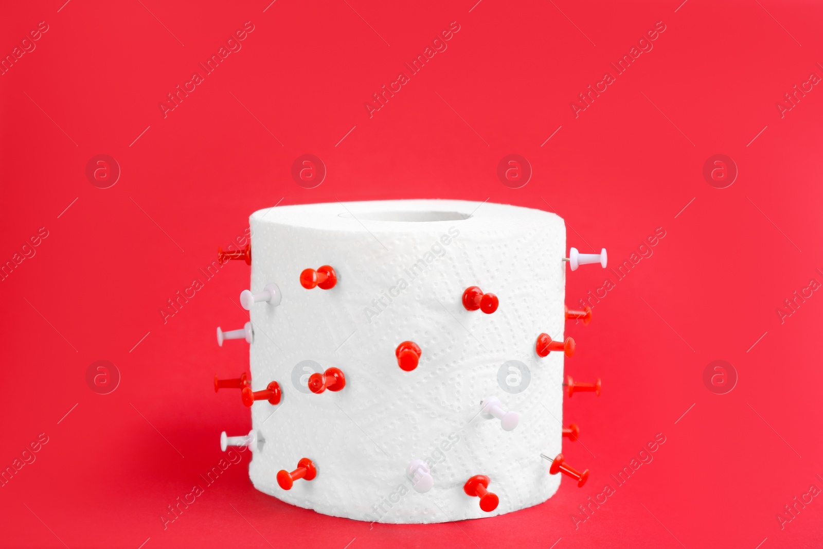Photo of Roll of toilet paper with pins on red background. Hemorrhoid problems