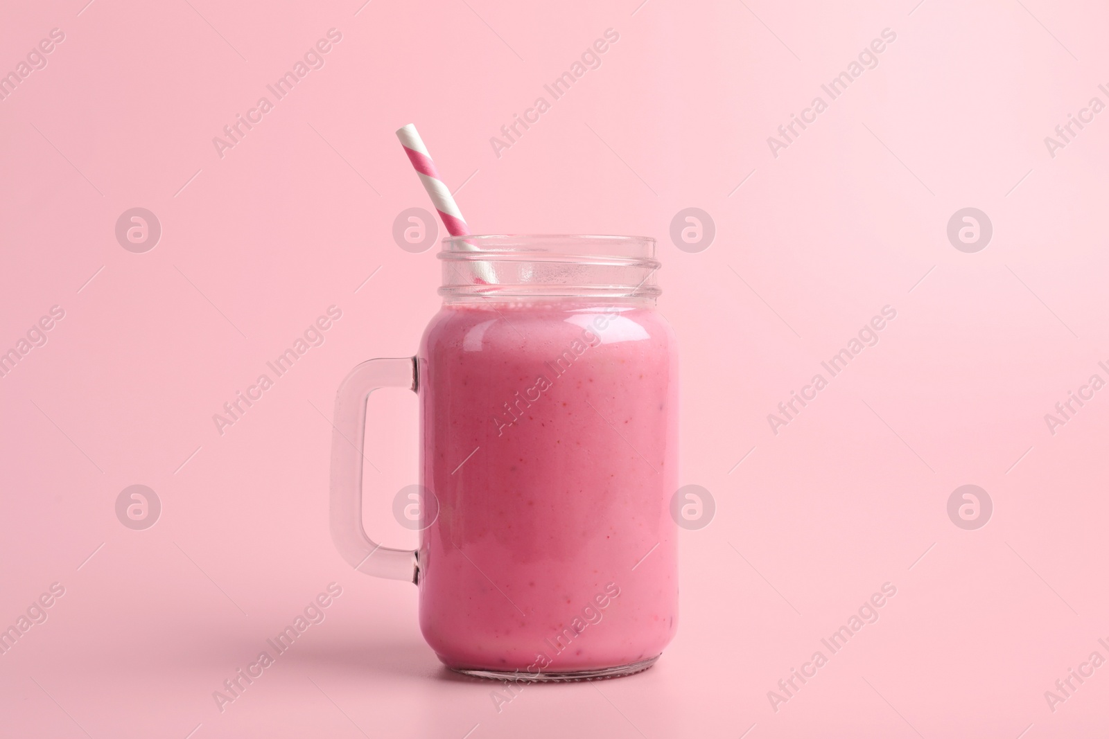 Photo of Mason jar with delicious berry smoothie on pink background