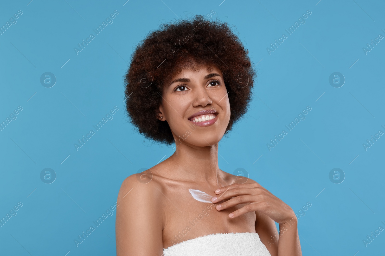 Photo of Beautiful young woman applying cream onto body on light blue background
