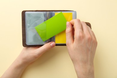 Woman holding business card holder with colorful cards on light yellow background, top view