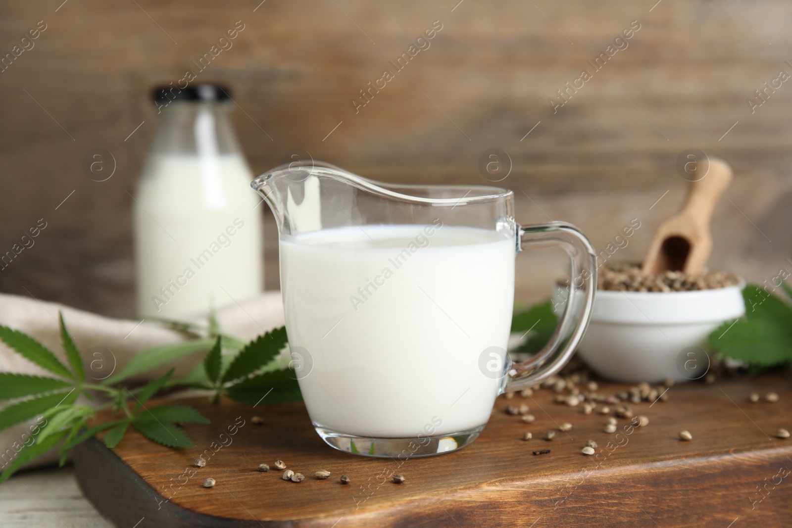 Photo of Glass jug with fresh hemp milk, seeds and leaves on wooden board