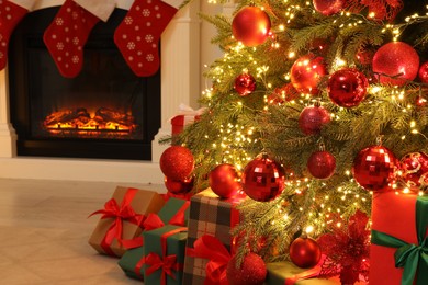 Many gift boxes under decorated Christmas tree and fireplace indoors