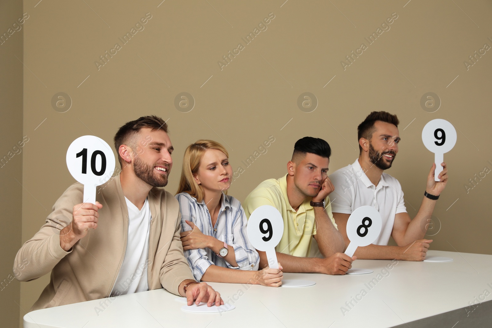 Photo of Panel of judges holding different score signs at table on beige background