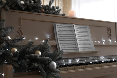 White piano with festive decor and note sheets indoors. Christmas music