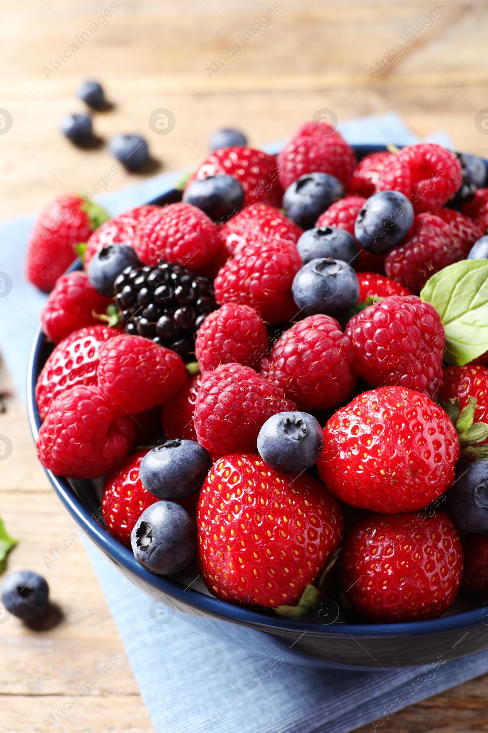 Photo of Different fresh ripe berries in bowl on wooden table, closeup