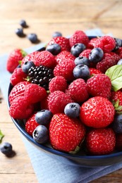 Different fresh ripe berries in bowl on wooden table, closeup