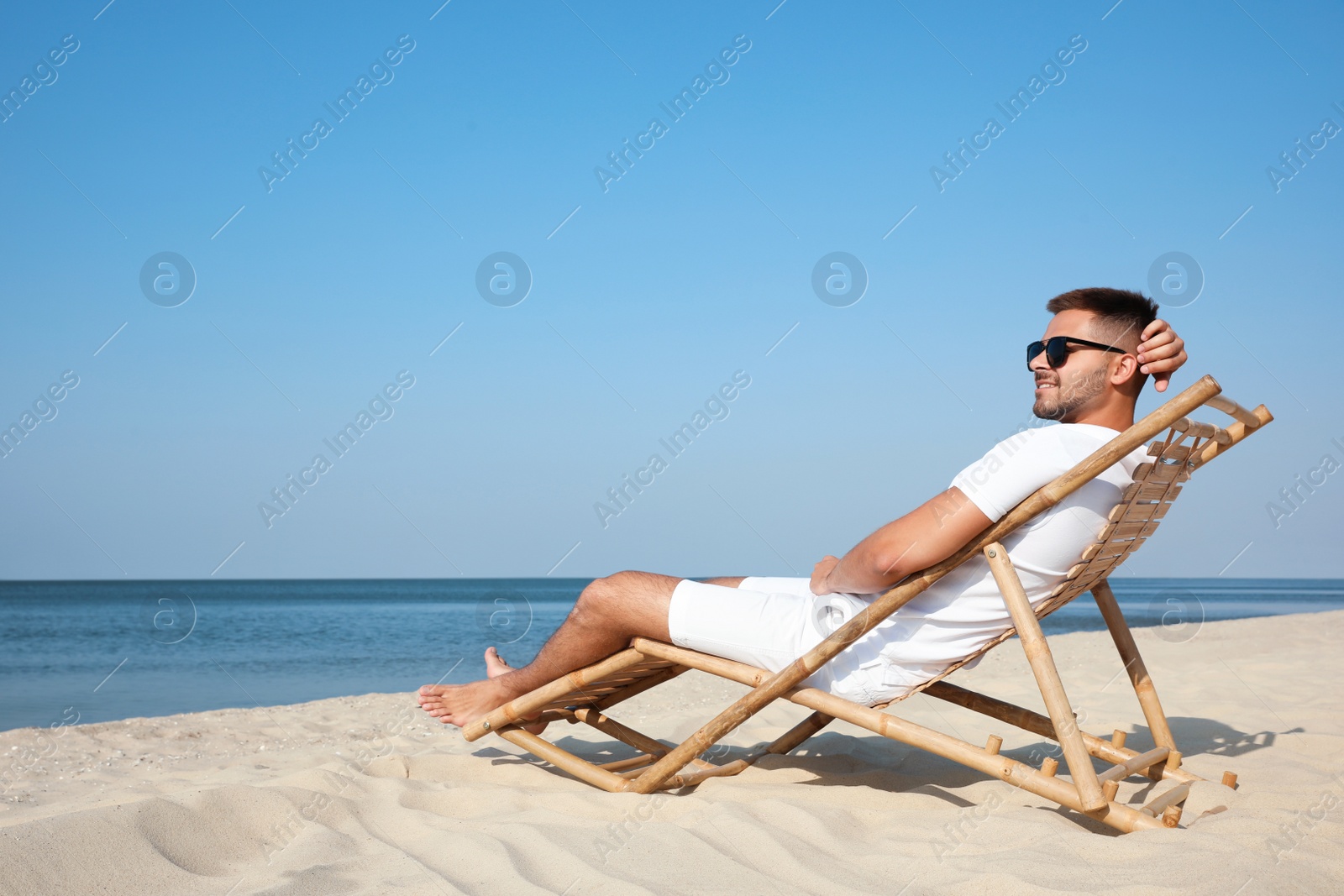 Photo of Young man relaxing in deck chair on sandy beach