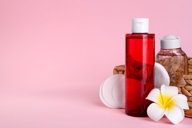 Photo of Bottles of micellar water, plumeria flower and cotton pads on pink background. Space for text