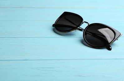 Photo of Stylish sunglasses on blue wooden background, space for text. Fashionable accessory