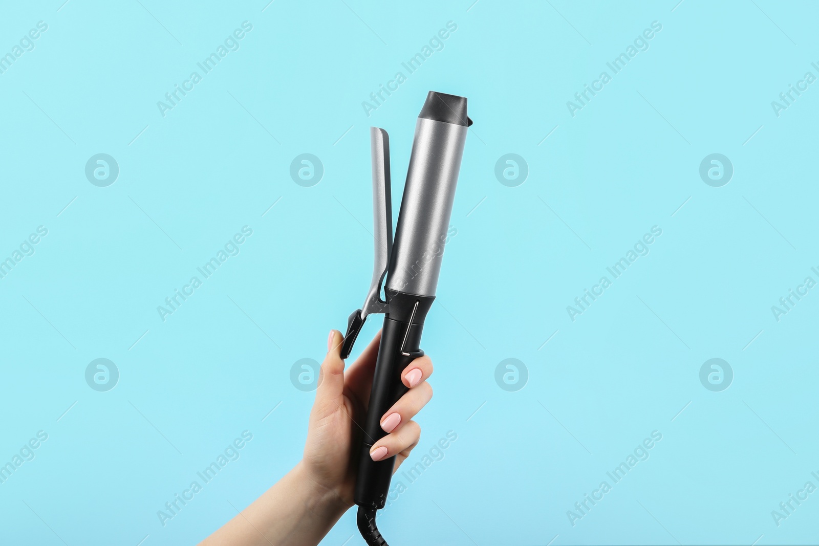 Photo of Hair styling appliance. Woman holding curling iron on light blue background, closeup